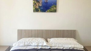 A neatly made bed with a grey quilt, two white pillows, and two rolled white towels tied with blue ribbons.
