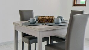 A dining table with four chairs, a woven bag, and two cups on placemats.
