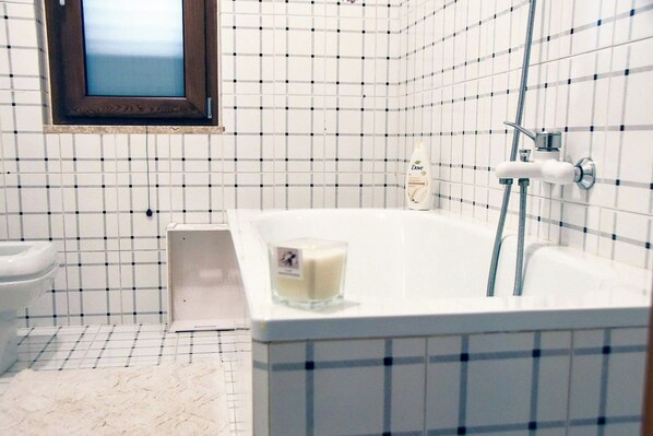 A bathroom with a white bathtub, a window, and a tiled wall.