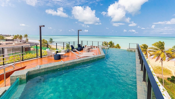 A pool with a view of the ocean, outdoor seating, and palm trees.