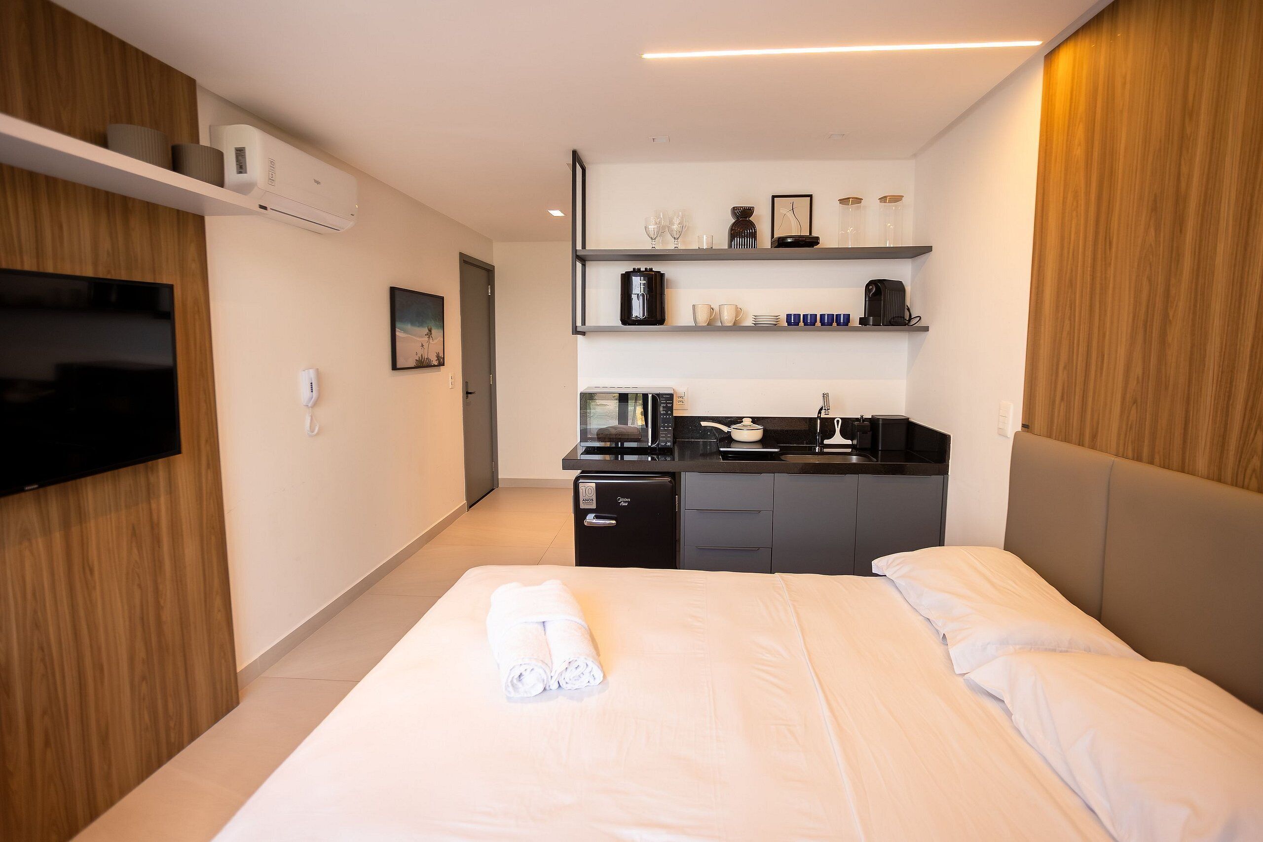 A hotel room with a bed, a TV, a kitchenette, and a wooden wall panel.