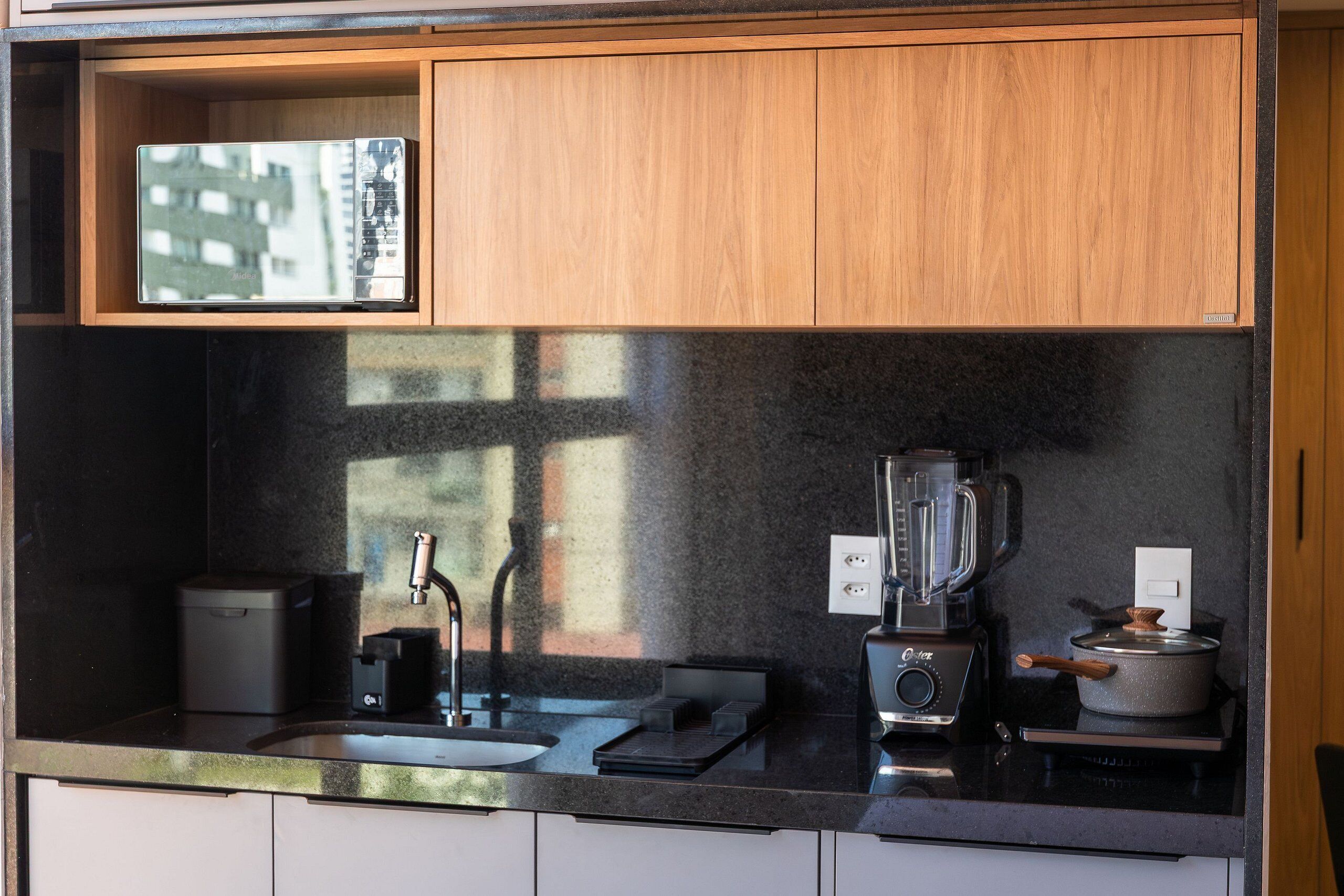 Una cocina con encimera negra, una licuadora, una olla en la estufa y un lavamanos pequeño.