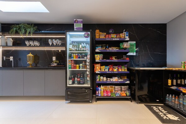 Un quiosco autoservicio con sección refrigerada, estantes para aperitivos y dispensador de agua.