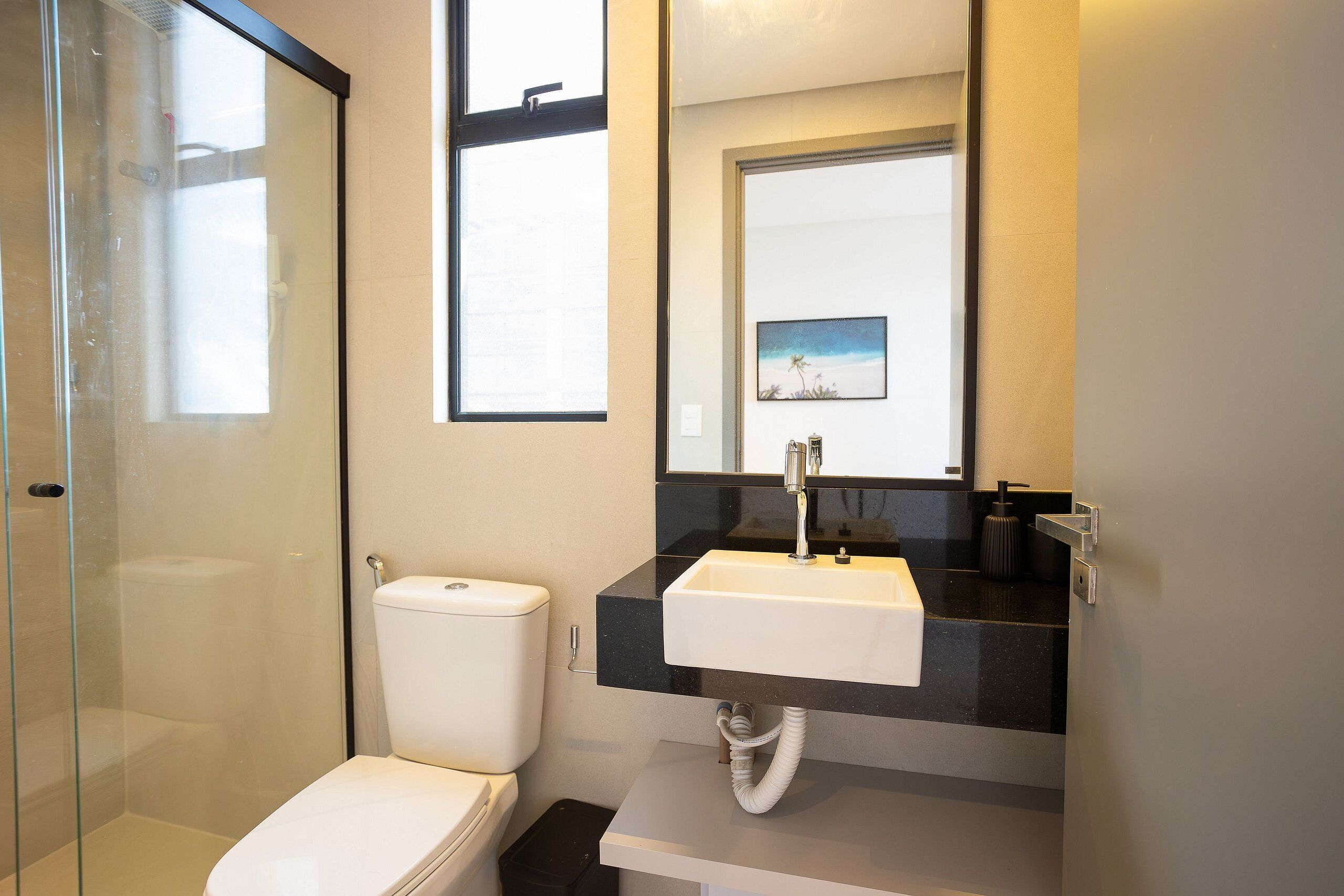 A bathroom with a glass shower enclosure, a white toilet, a black countertop sink, and a mirror above the sink.