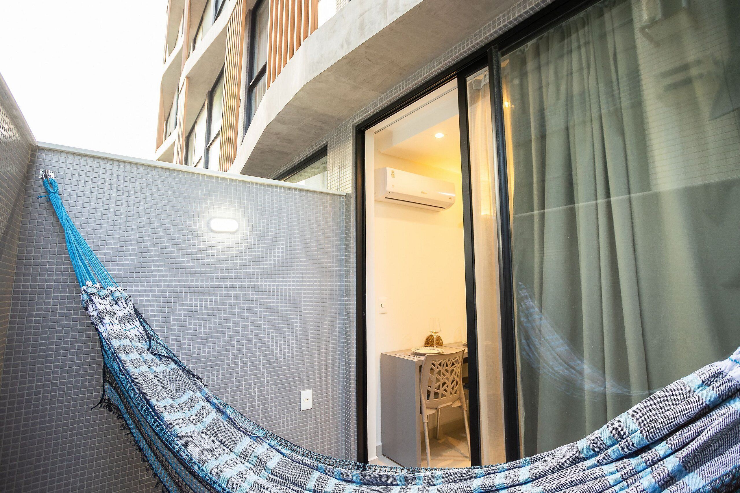 A hammock in a corner, a window with curtains, and a small table with a chair.