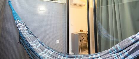 A hammock in a corner, a window with curtains, and a small table with a chair.