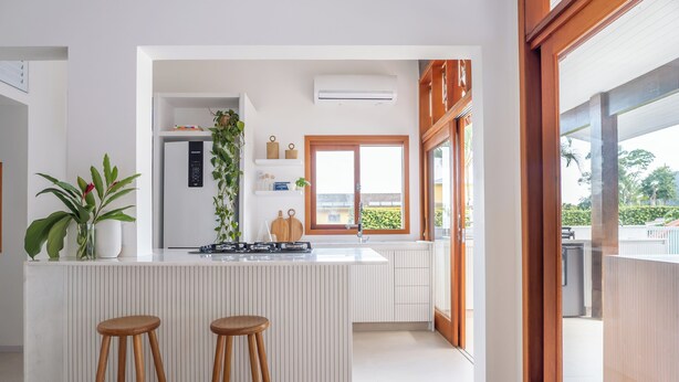 Une cuisine moderne avec un îlot central, des tabourets en bois et une vue dégagée grâce à une grande fenêtre.