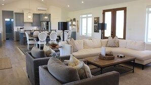 A spacious living area with a large sofa, two armchairs, a coffee table, and a dining table with chairs. There is a kitchen in the background with cabinets and a refrigerator. - Water View Vacation Home Located in Rustico- Subdivision Access To Beach. (Rustico)