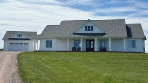 A large, single-story house with a garage, a covered porch, and a well-maintained lawn. - Water View Vacation Home Located in Rustico- Subdivision Access To Beach. (Rustico)