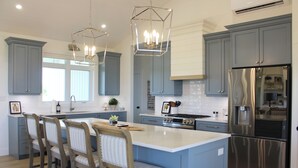 A modern kitchen with blue cabinets, a large island with bar stools, stainless steel appliances, and pendant lighting. - Water View Vacation Home Located in Rustico- Subdivision Access To Beach. (Rustico)