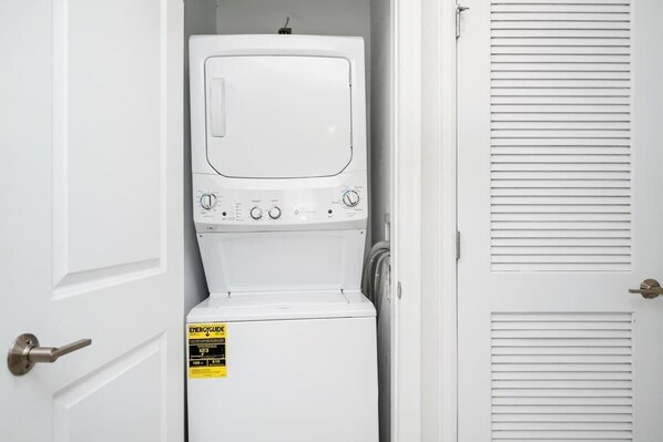 A white washer and dryer unit with an ENERGYGUIDE sticker, located in a room with white doors and louvered windows.