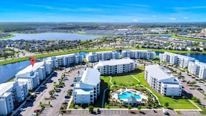 Un moderno complejo residencial con varios edificios de apartamentos, una piscina central y un lago al fondo.