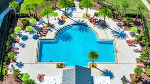 Luftaufnahme eines Resorts mit einem zentralen Swimmingpool, umgeben von Liegebereichen mit Liegen und Sonnenschirmen sowie Palmen.