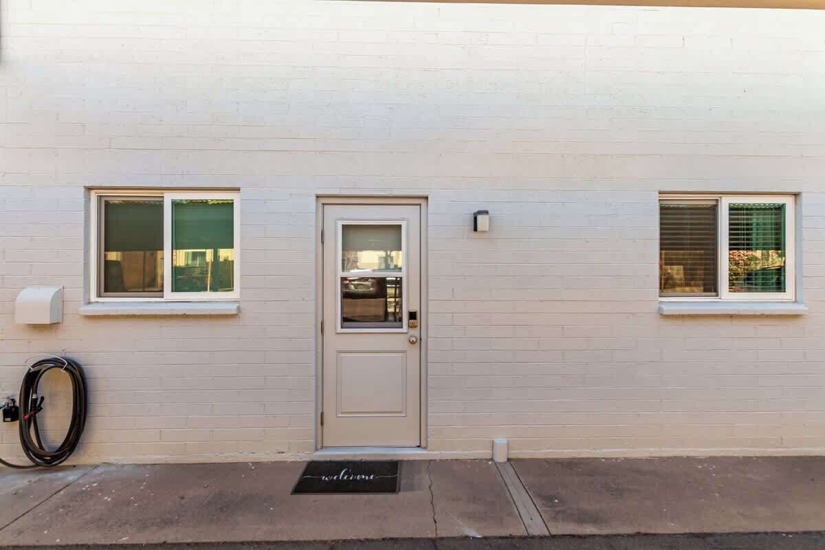 Un bâtiment à l’extérieur blanc, avec une porte d’entrée et deux fenêtres équipées de stores.