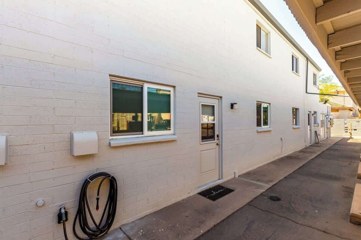 Un bâtiment blanc doté d’un espace extérieur couvert, d’un tuyau d’arrosage et d’une porte.