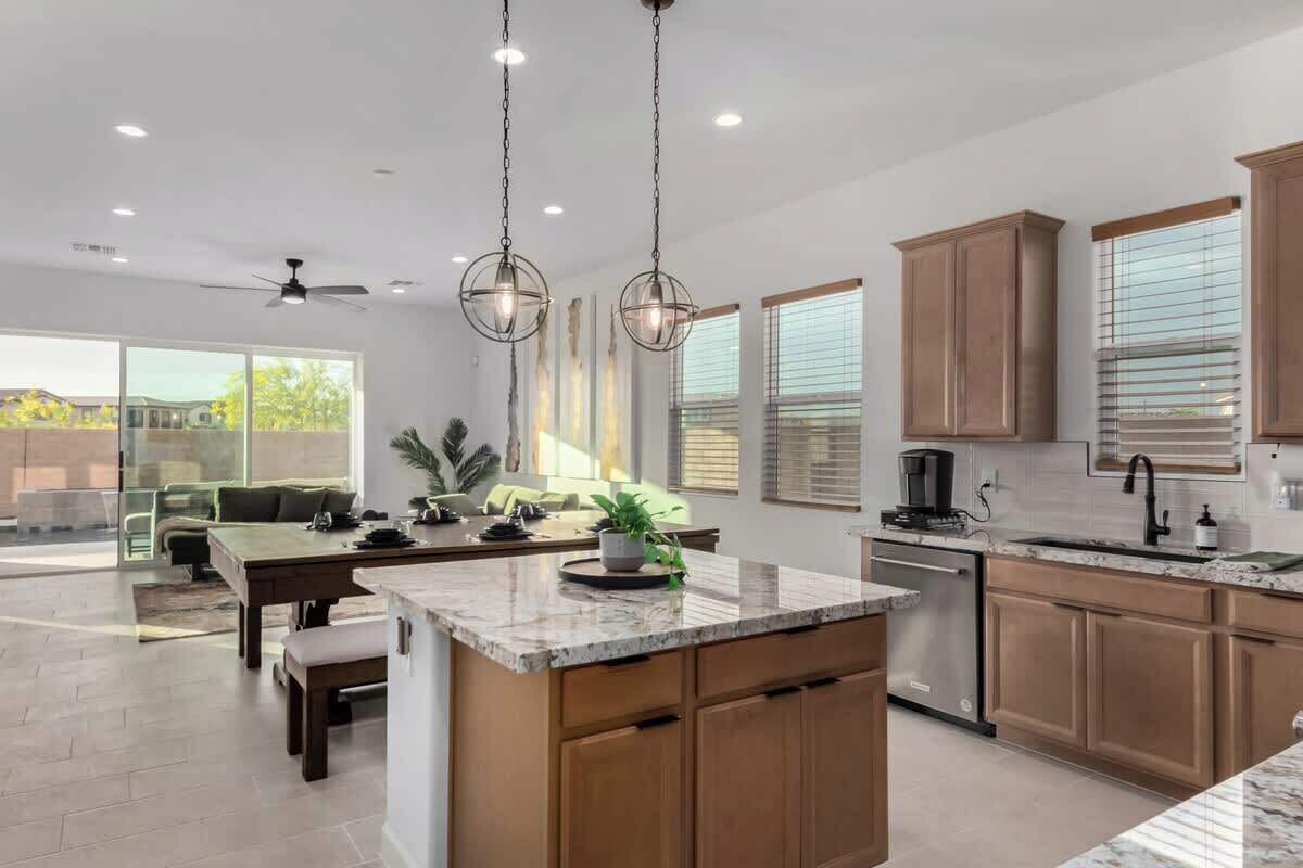 A modern kitchen with wooden cabinets, a marble countertop, and pendant lighting.