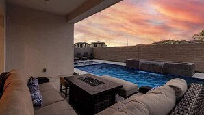 A modern outdoor pool area with a view of the sunset, a lounge with a fire pit, and a brick wall. - Luxe 4BR Retreat w/ Pool, Hot Tub & Sunset Views (Goodyear)
