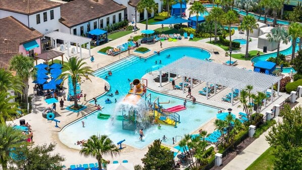 A large outdoor swimming pool with multiple lanes, a water slide, and a children's play area.