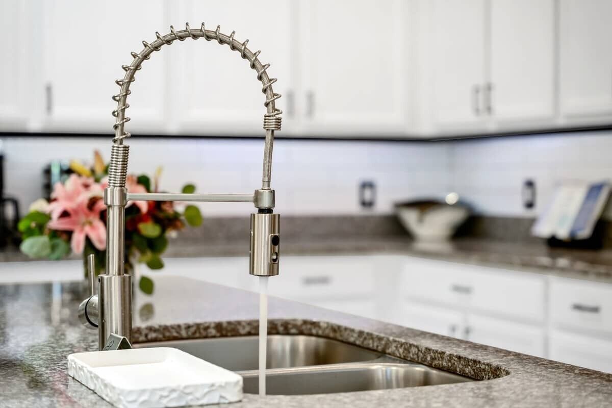 Una cucina moderna con un design del rubinetto originale, un piano di lavoro in granito e mobili in legno bianco.
