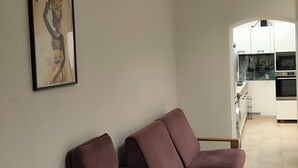 A modern living room with two sofas, a kitchen in the background, and a framed artwork on the wall.