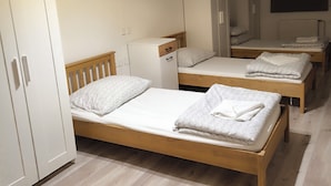 A compact bedroom with two wooden beds, a wardrobe, a small cabinet, and a ceiling light fixture.