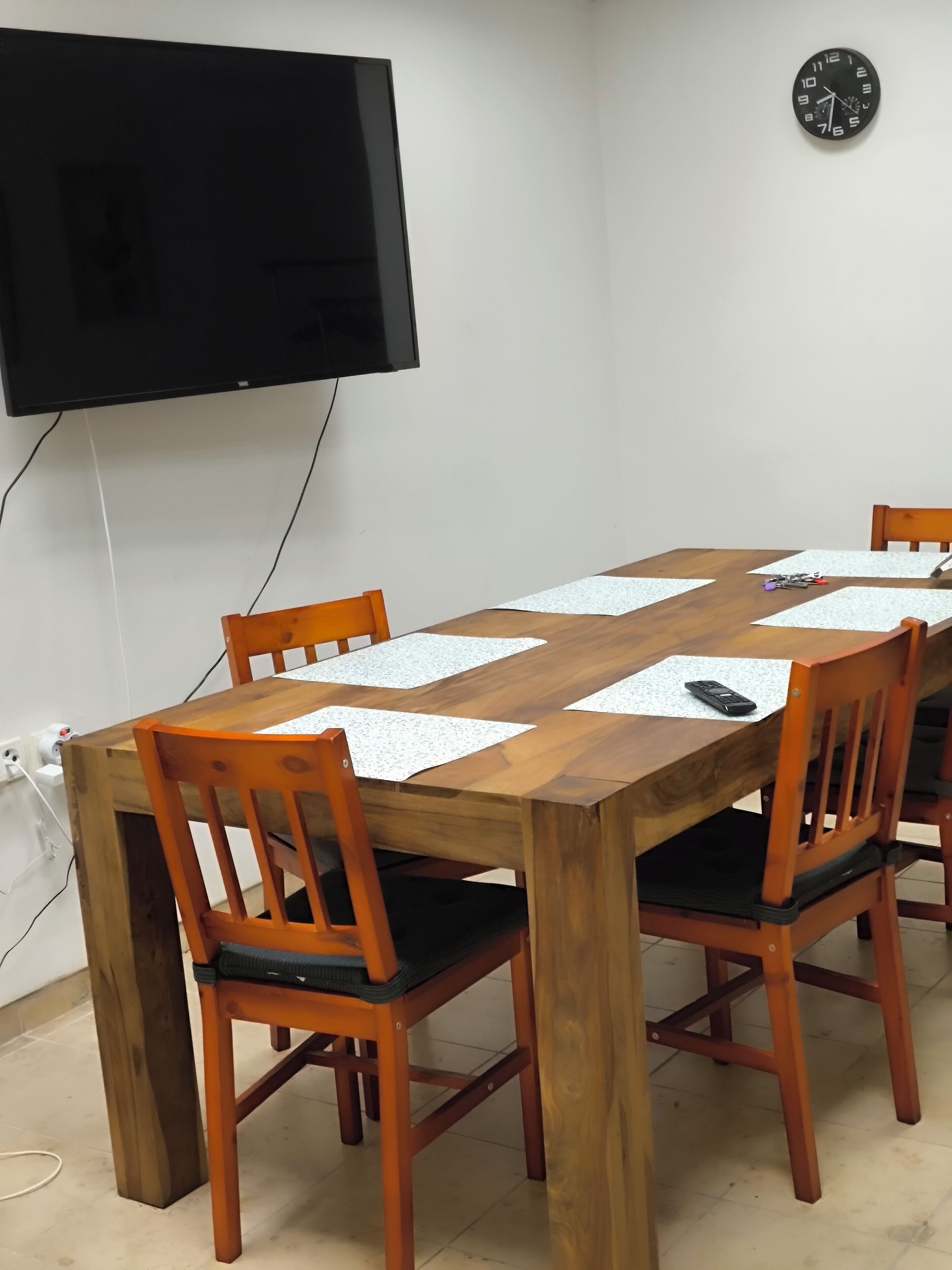 Un salón de conferencias con una mesa de madera, seis sillas, un televisor negro montado en la pared y un reloj en la pared.