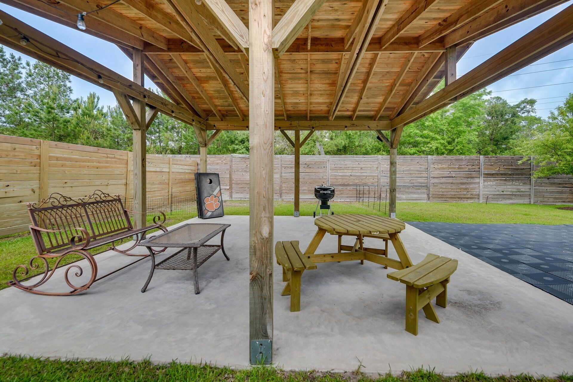 A covered outdoor patio with a concrete floor, a metal bench, a picnic table, and a grill.