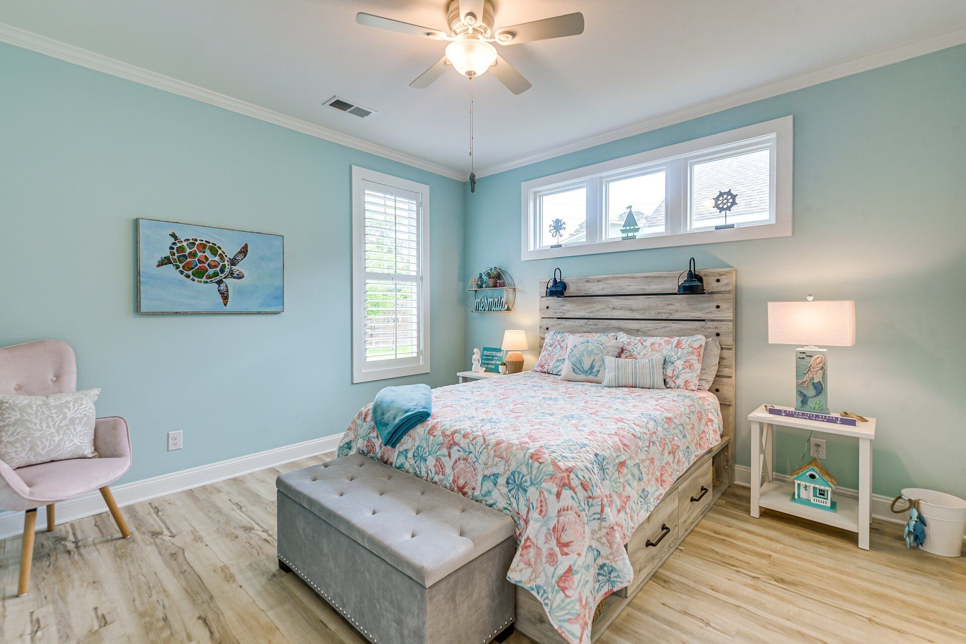 A bedroom with a bed, a chair, a nightstand, a lamp, and a ceiling fan.