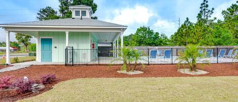 A single-story building with a covered porch, a small pool area with lounge chairs, and a fenced-in area with palm trees.
