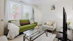 Ein modernes Wohnzimmer mit einem grünen Sofa, einem weißen Sessel, einem Glastisch und einem Flachbildfernseher.