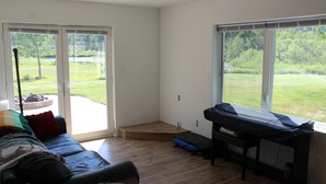 Une pièce dotée d’un plancher en bois, d’un canapé, d’un banc et de grandes fenêtres donnant sur un espace verdoyant.