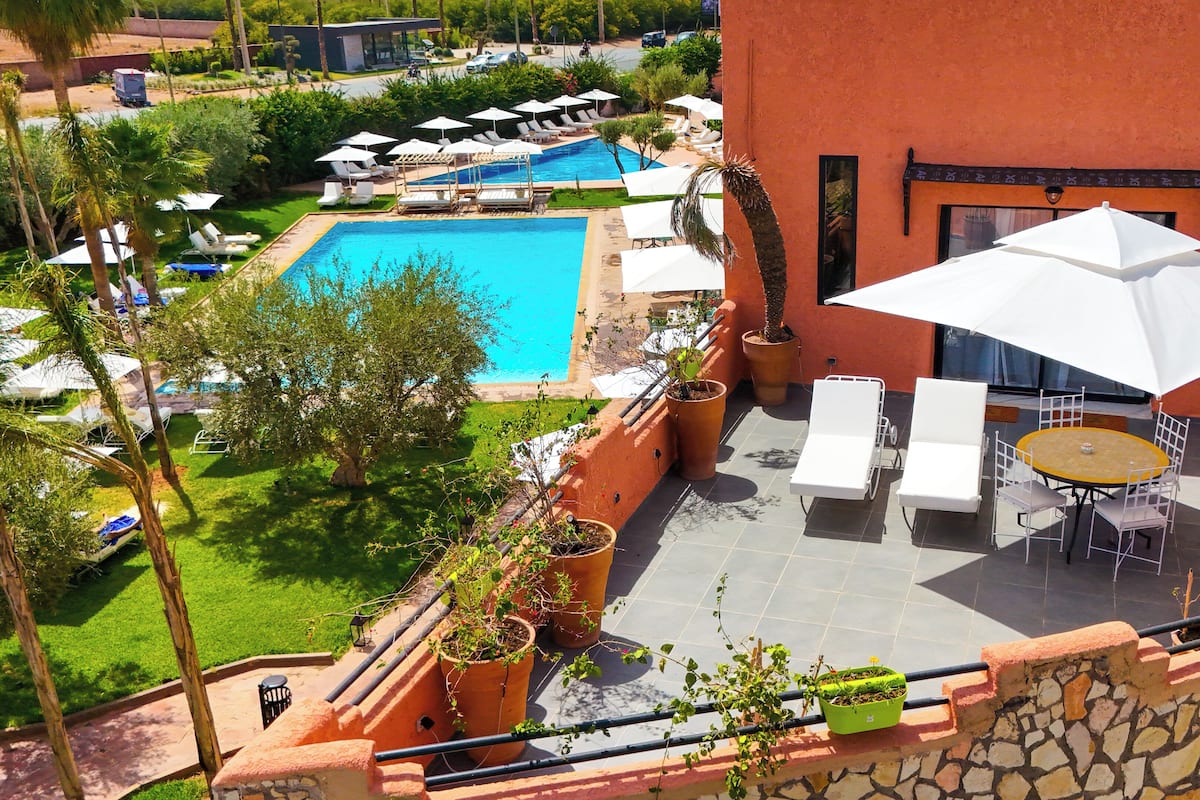 A rooftop pool area with lounge chairs and umbrellas, surrounded by potted plants and a stone wall.