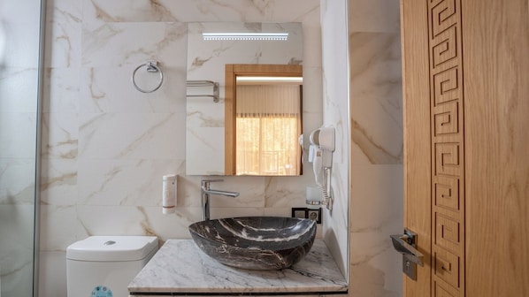 Un baño con lavamanos de mármol, inodoro, espejo y ducha.