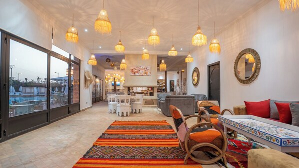 A spacious living area with a large window, a dining area with chairs and a table, and a seating area with sofas and a patterned rug. - Ourika Camp Suites Hotel & Resort  (Marrakech)