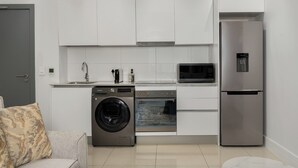 Une cuisine moderne avec des meubles blancs, un réfrigérateur en acier inoxydable, un four à micro-ondes, un lave-linge et un four.
