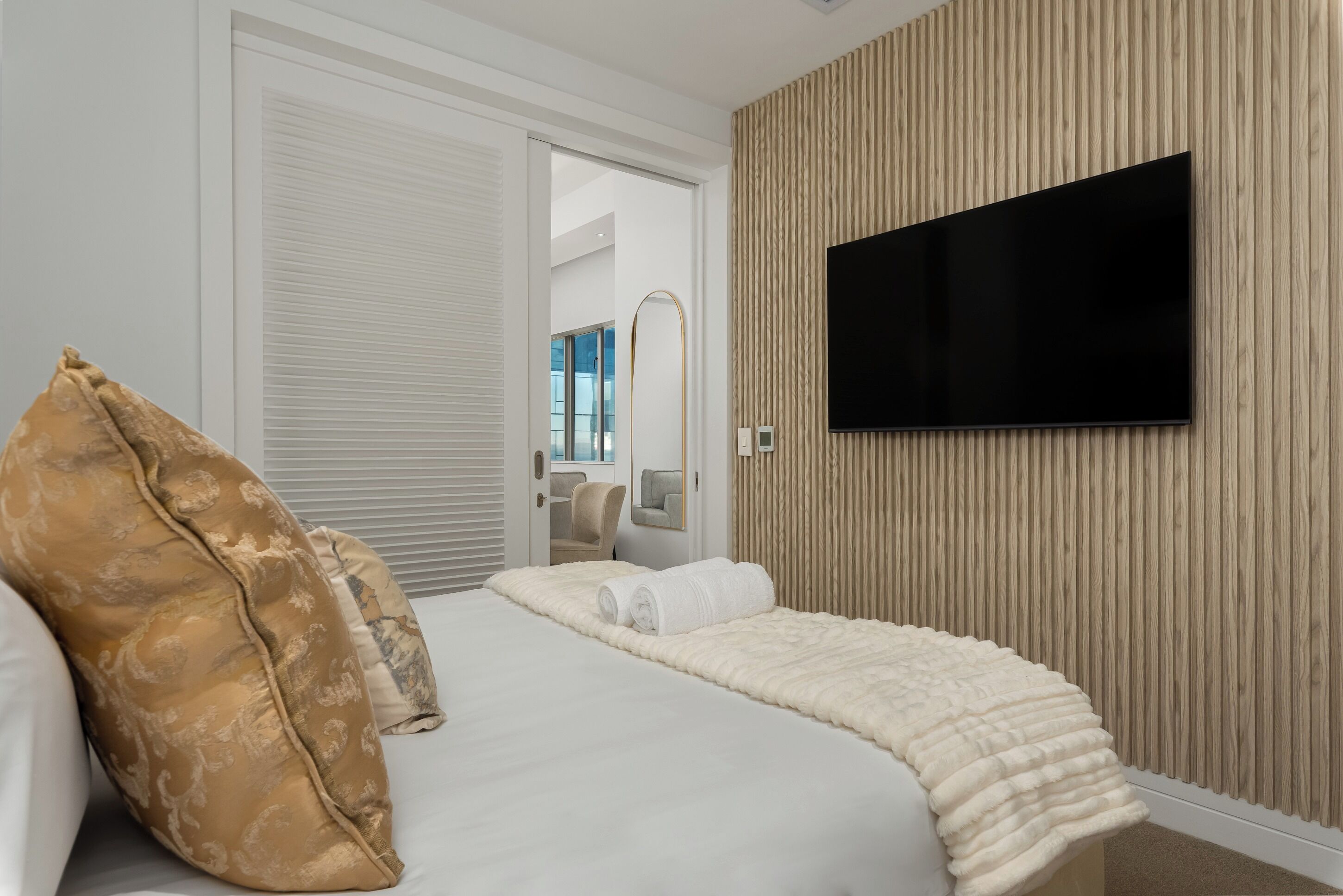Quarto de hotel moderno com uma cama grande, televisão de tela plana na parede e design em painel de madeira.