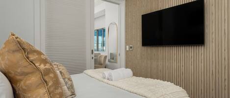 Quarto de hotel moderno com uma cama grande, televisão de tela plana na parede e design em painel de madeira.