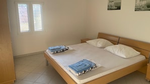 Ein Schlafzimmer mit einem hölzernen Bett, weißer Bettwäsche und zwei Fenstern mit Jalousien.