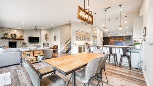 A modern kitchen with a wooden dining table, bar stools, and pendant lighting.