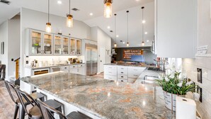 A spacious kitchen with a large granite island, white cabinetry, and pendant lighting.