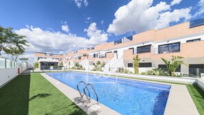 Un immeuble résidentiel moderne doté d’une piscine, de pelouses verdoyantes et surplombant un ciel bleu azur.