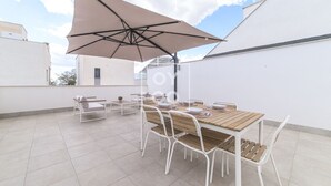 A rooftop patio with a wooden table and chairs, a large umbrella, and a white wall in the background. - Perla de Pilar - Private pool and rooftop near Beach - by Oyoostays (Pilar de la Horadada)