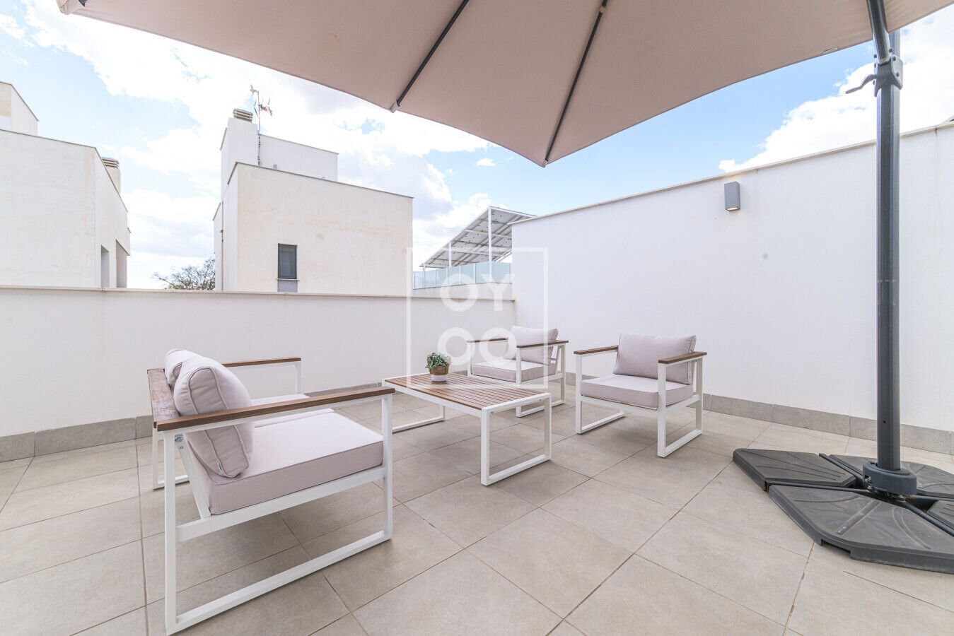 Une terrasse sur le toit avec une table, deux chaises et un grand parasol.