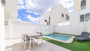 A modern outdoor patio with a pool, a table with chairs, and a lounge chair. - Perla de Pilar - Private pool and rooftop near Beach - by Oyoostays (Pilar de la Horadada)