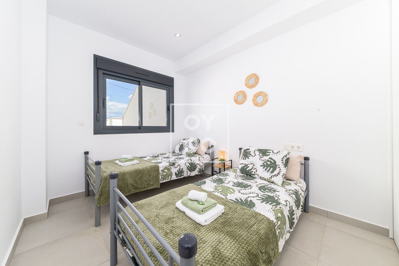 A bedroom with two single beds, a window, and a small bedside table with a lamp.