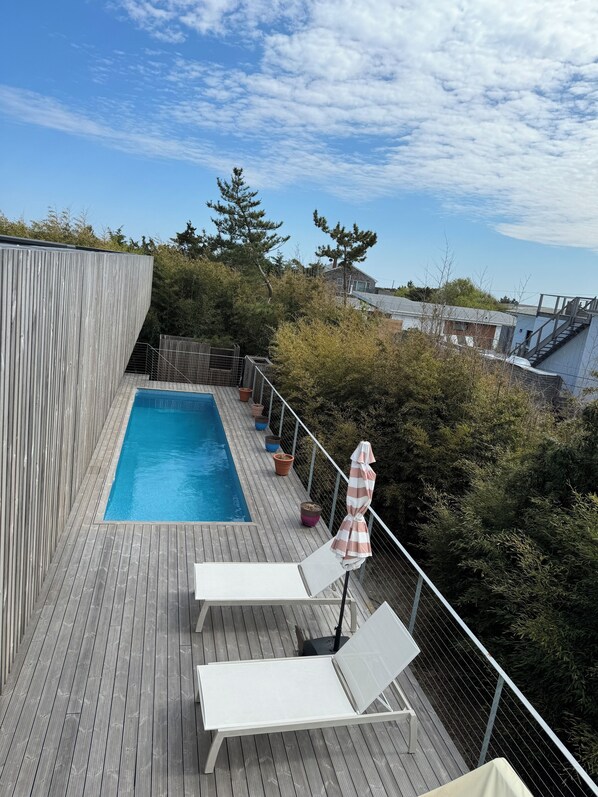 Une terrasse en bois avec une piscine, deux chaises longues et un petit parasol.