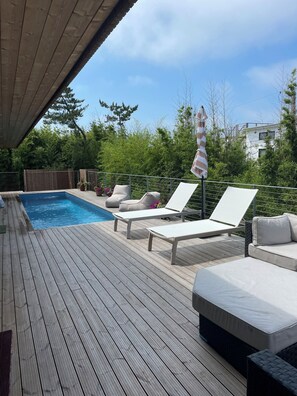 Une terrasse en bois avec une piscine, des chaises longues et un espace abrité.