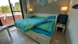 Relax in this serene bedroom with a large bed, nightstand, and a window offering a view of lush greenery.