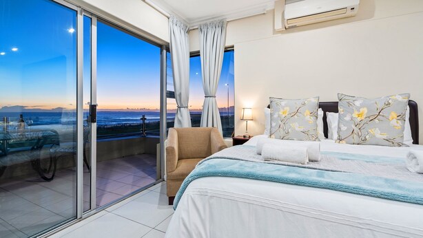 Ein Hotelzimmer mit einem großen Bett, einem Sessel, einem Nachttisch und Blick auf den Ozean.