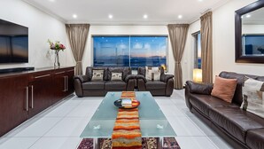 Ein modernes Wohnzimmer mit einer Couch, einem Glastisch, einem Fernseher und Blick auf die Stadtlandschaft.